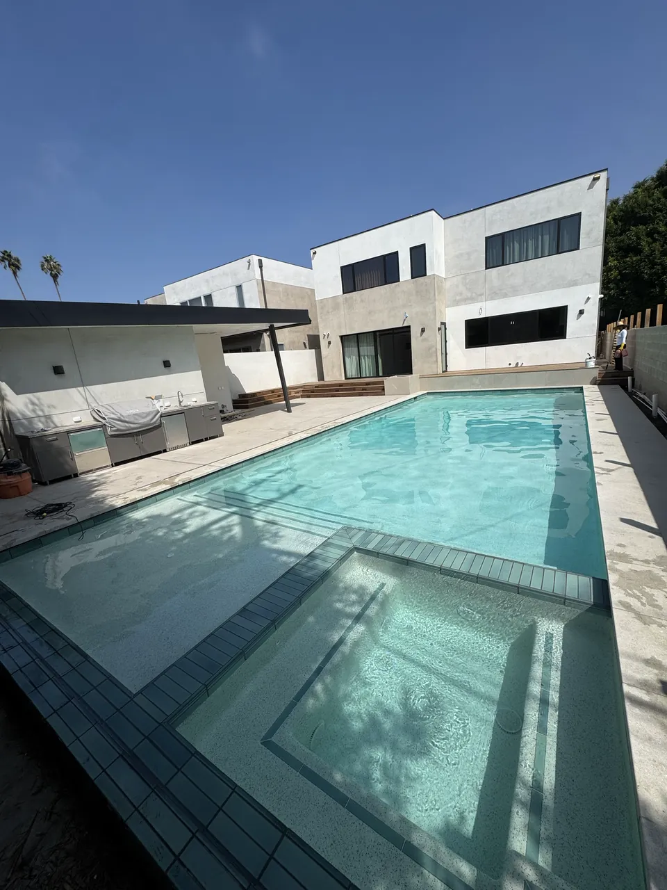 Modern pool and attached spa with gray tile edging beside a contemporary home